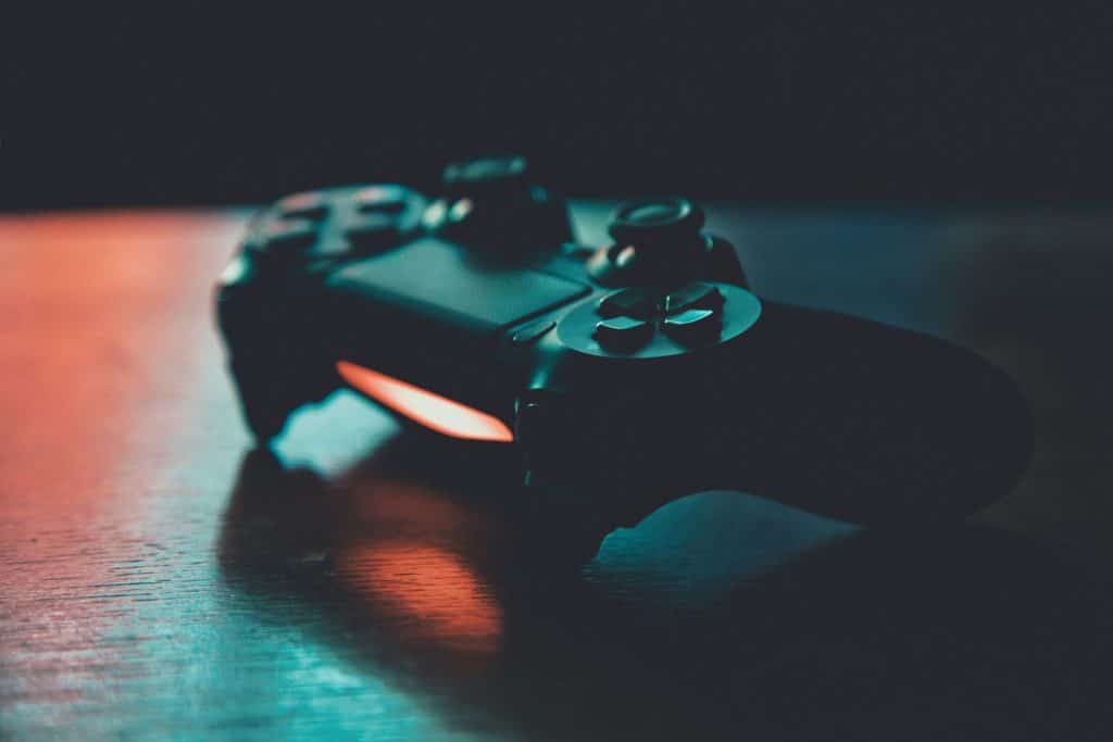Dunkler Gamecontroller auf einem Holztisch, beleuchtet von rotem und türkisem Licht